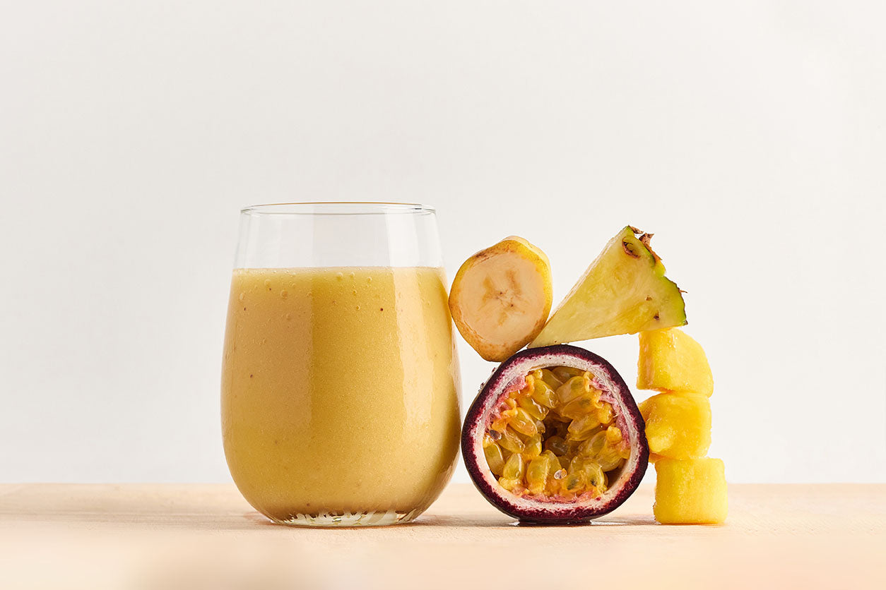 Healthy smoothie in glass with banana pineapple mango and passionfruit ingredients next to it