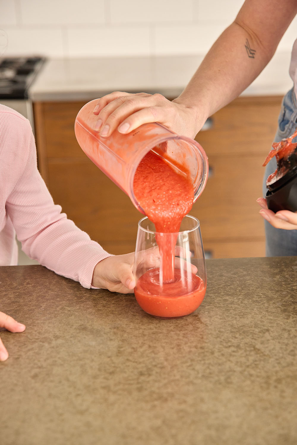 Parent pouring healthy berry smoothie into glass for child in kitchen